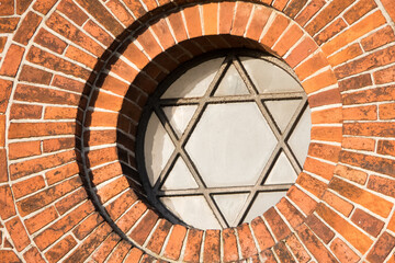 View of a pentagram sign and symbol on an old round window on a red brick wall. Vintage glass with...