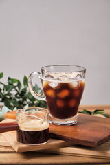 cold iced black brew coffee in a glass with pieces of ice on a wooden table, natural light, fresh summer drink in the morning