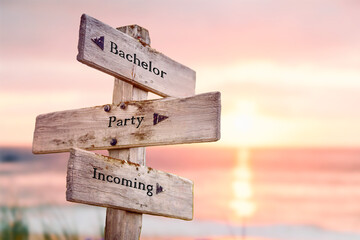 bachelor party incoming text quote on wooden crossroad signpost outdoors on beach with pink pastel...