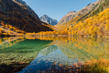 Lake with transparent water and autumnal trees. Mountains and lake