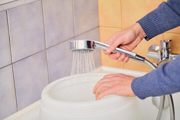 Hands pour water into plastic container through  hose with nozzle