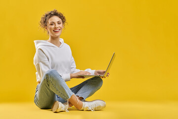 Smiling female student in casual clothes, surfing internet on laptop inside. Front view of girl...
