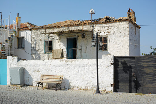 An Old White Farmhouse Exterior. Ancient Rustic House On The Street With A Broken Damaged Roof, Tiny Square Windows And Brick Walls. Open Windows In Thick Stone Wall Of An Weathered Antique Building