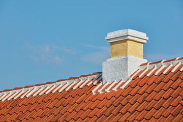 Fototapeta premium Brick chimney designed on slate roof of house building outside against blue sky background. Construction of exterior architecture of escape chute built on rooftop for fireplace smoke and heat