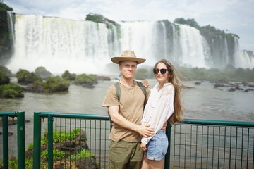 In the photo, a beautiful girl and a guy stand against the backdrop of Iguazu Waterfalls located on the border of Brazil (Paran&aacute; state) and Argentina (Misiones province).