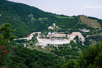 Fototapeta na wymiar Quarry for extraction of minerals with equipment and machines, and road, in Rhodope Mountains covered with forests