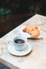 Cup of coffee and a croissant for breakfast on a table in a street cafe.