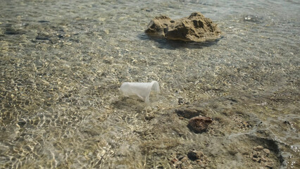 Transparent plastic cup is carried away by the wind to the sea in the coastal zone. Plastic pollution of the surf zone. Red sea, Egypt