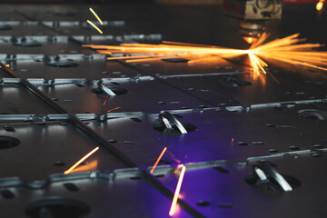Laser cutting machine, with a bright flash and sparks, cuts out details from a sheet of steel,...