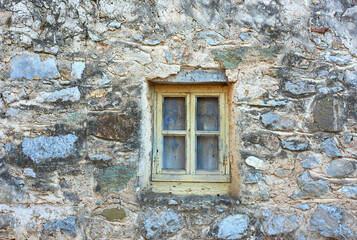 Fototapeta na wymiar Wooden window on an old rough stone wall farmhouse or ancient house. Vintage, rustic, old fashioned frame on historic village building and background. Architecture antique structure with background