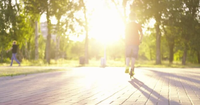 Child with kick scooter. Young boy riding on scooter on path in the park in summer. Kids leisure activity, sport