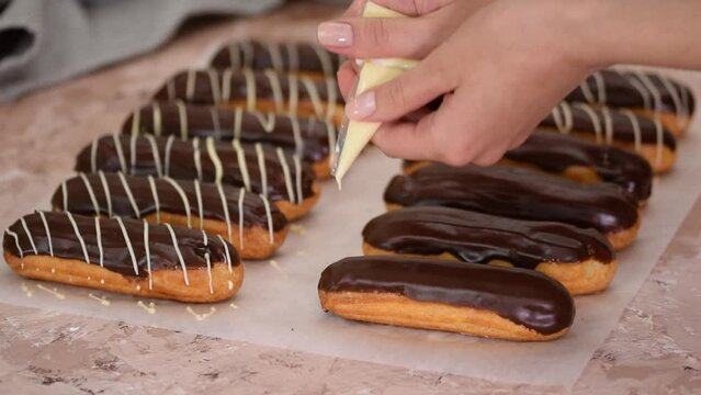 Pastry chef pours white chocolate on French eclairs.