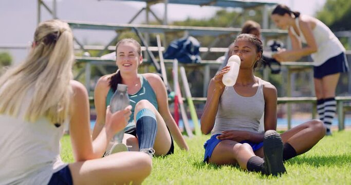 Group of young fit sporty female hockey players drinking water during a break from practice. Athletic young female teammates hydrating for a game outside. Preparing to go on a sports court to play