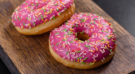 A beautiful doughnut with pink glaze and colored sprinkle on a dark concrete background