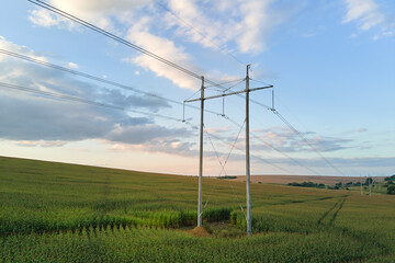 High voltage tower with electric power lines between green agricultural fields. Transfer of...