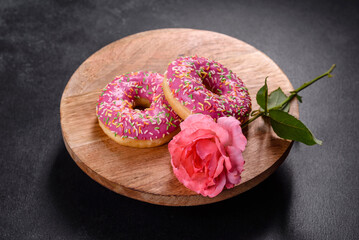 A beautiful doughnut with pink glaze and colored sprinkle on a dark concrete background