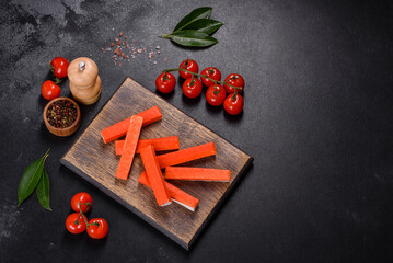 Crab sticks on a cutting Board with a knife. On black concrete background © chernikovatv