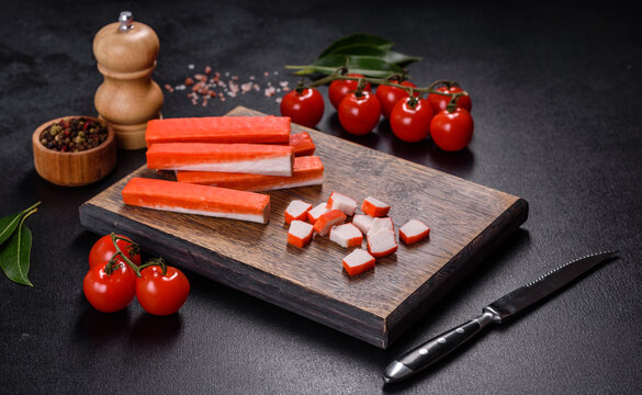 Crab sticks on a cutting Board with a knife. On black concrete background