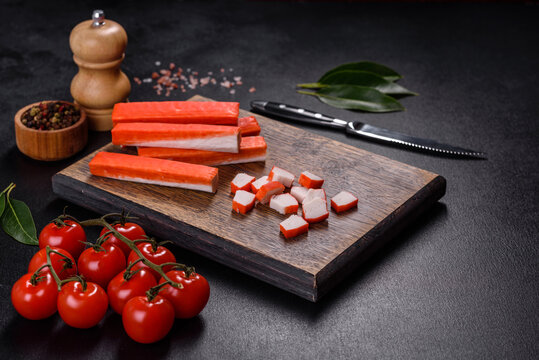 Crab sticks on a cutting Board with a knife. On black concrete background