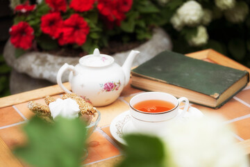 porcelain teapot into a cup on a vintage table in the garden against a background of flowers and an old book in summer