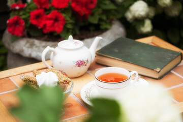 porcelain teapot into a cup on a vintage table in the garden against a background of flowers and an...