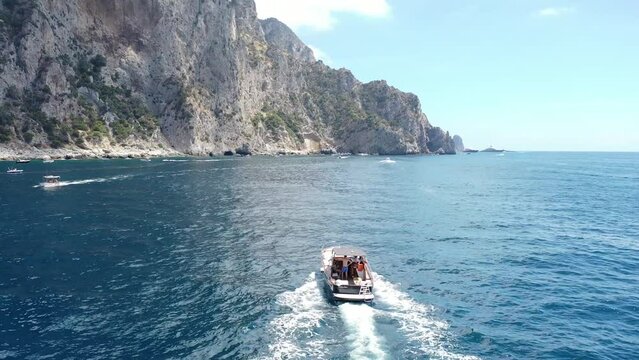 Aerial Drone Footage Above Boats as they Approach Capri, Italy, along the Cliffs and Coast in the Summer