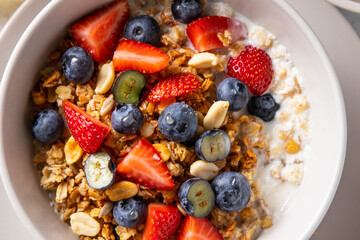 Homemade granola with yogurt or milk, blueberry, strawberry and honey in bowl on grey background. Healthy breakfast. Selective focus.