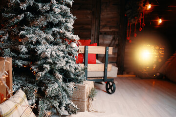 Christmas tree in snow, garland, gift boxes, wooden trolley with pillows and decorations in New Year's interior of photo studio. Festive atmosphere.