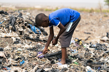 Young black boy poking aroung with a stick in a huge mountain of garbage at a landfill in West...