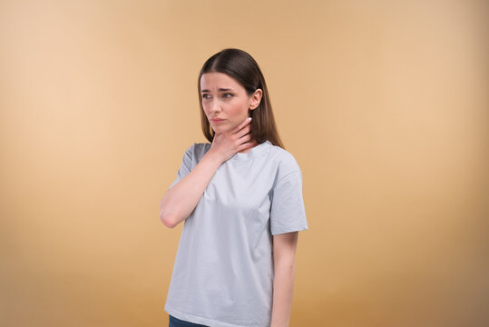 Young lady suffering from sore throat on a beige background