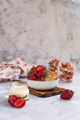 Tiramisu summer dessert with fresh strawberries and cream in a glass on a light gray marble background. Strawberry cream dessert in glasses, white background.