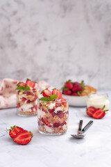 Tiramisu summer dessert with fresh strawberries and cream in a glass on a light gray marble background. Strawberry cream dessert in glasses, white background.