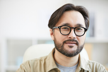 Fototapeta na wymiar Close-up of content intelligent young Asian man with beard wearing eyeglasses working in office