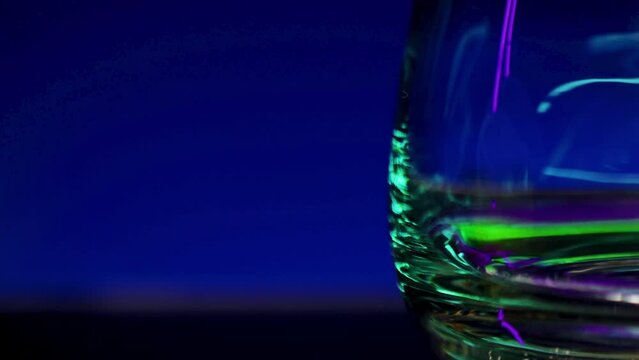 Close up of empty transparent glass with the reflection of lights. Stock clip. Wall with colorful illumination of a night bar.