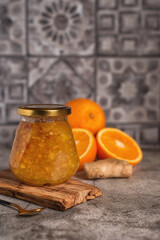 Homemade jam. A glass jar of orange-ginger jam on a gray background. Homemade orange and ginger marmalade and fresh oranges and ginger on the gray kitchen table.