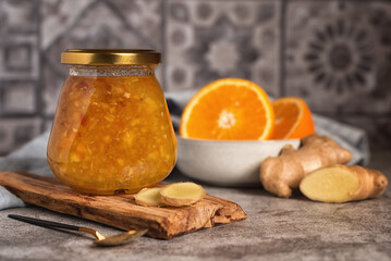 Homemade jam. A glass jar of orange-ginger jam on a gray background. Homemade orange and ginger...