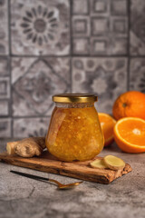 Homemade jam. A glass jar of orange-ginger jam on a gray background. Homemade orange and ginger marmalade and fresh oranges and ginger on the gray kitchen table.