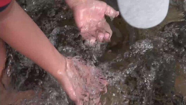 child plays with hands in a mountain river