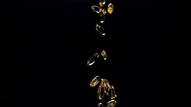 Capsules of vitamin omega 3 fall on the table. On a black background. Filmed on a high-speed camera at 1000 fps.