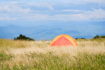 An orange tent in a meadow with sweeping views of the Appalachian Mountains