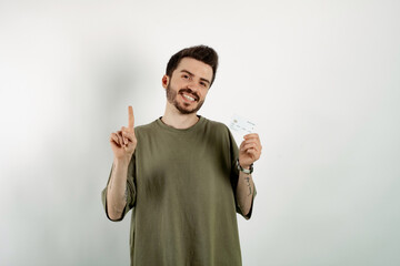 Happy casual man wearing t-shirt posing isolated over white background holding credit card and pointing with hand and finger to the side.
