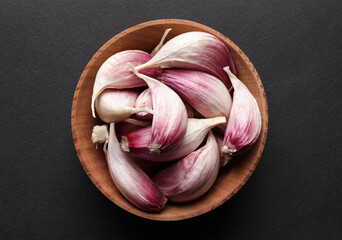 Unpeeled garlic cloves in wooden bowl on black background, top view - Powered by Adobe