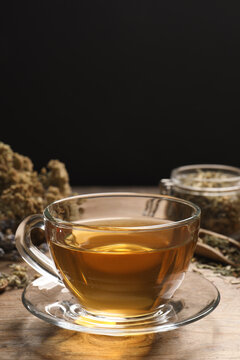 Freshly brewed tea and dried herbs on wooden table against black background. Space for text
