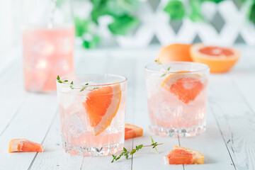 Glasses of grapefruit spritzer with thyme against a light airy background.