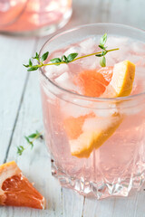 Close up of a grapefruit spritzer garnished with a grapefruit slice and thyme.