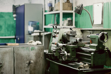 Fototapeta premium Small green metalworking lathe with lamp and sketch attached on metal board in factory workshop