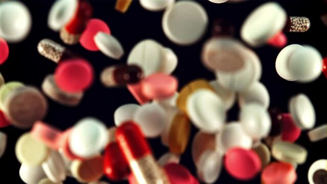 Various pills and capsules rise up and fall down. On a black background. Top view. Filmed is slow motion 1000 fps.