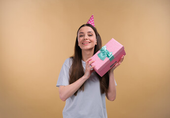 Happy young cheerful birthday girl with a present wearing party head on a beige background.