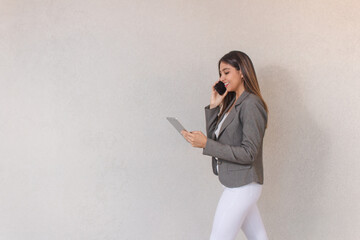 Beautiful business girl walking while talking on phone and using tablet on white background.