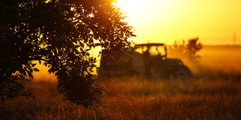 Making hay - tractor on a pasture against the setting sun  - 512870028